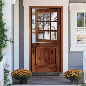 Farmhouse-style wooden front door with glass panes, surrounded by white trim and potted flowers on a porch